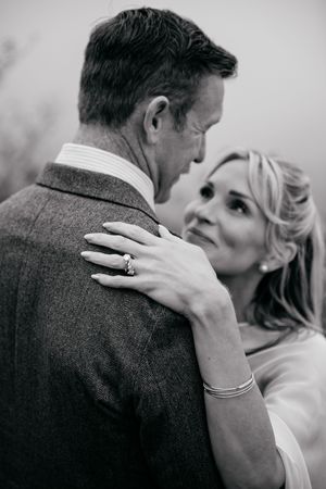 Black and white photo of a couple embracing, woman gazing up lovingly at man, wearing an engagement ring and bracelet.