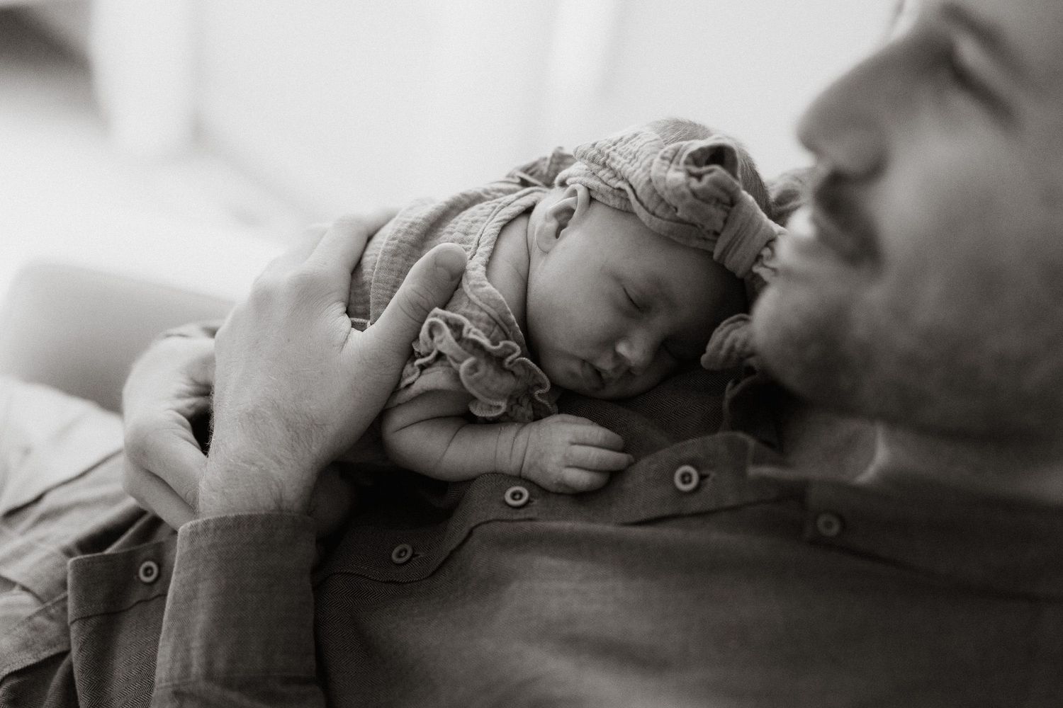Black and white photo of a sleeping newborn baby resting peacefully on a father's chest.