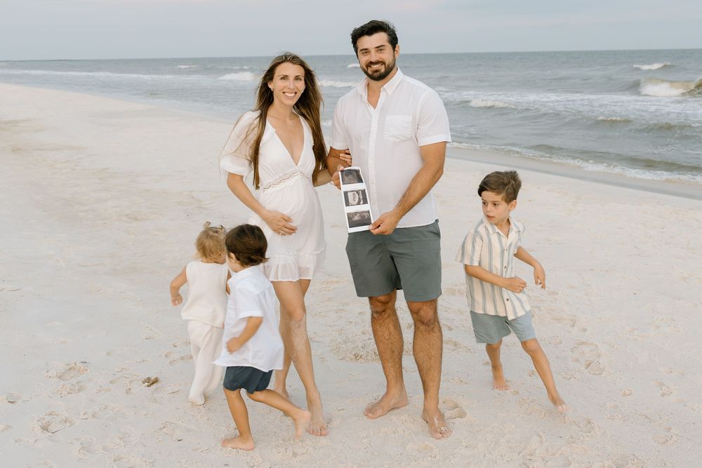 Family pregnancy announcement session on the beach in Orange Beach, Alabama, with mom holding an ultrasound photo.