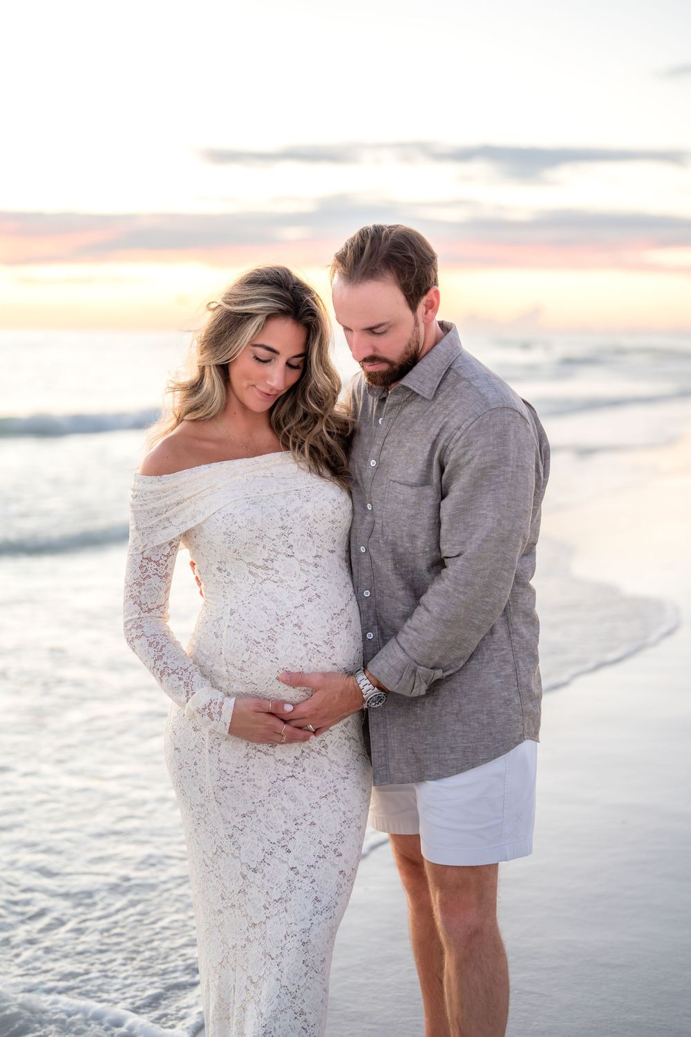 A couple shares a tender moment on the beach at sunset, cradling the woman's pregnant belly.
