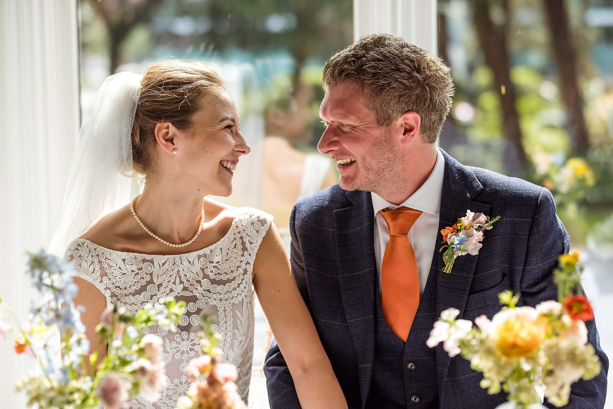 Happy bride and groom laughing together at their wedding ceremony, surrounded by colorful floral arrangements.