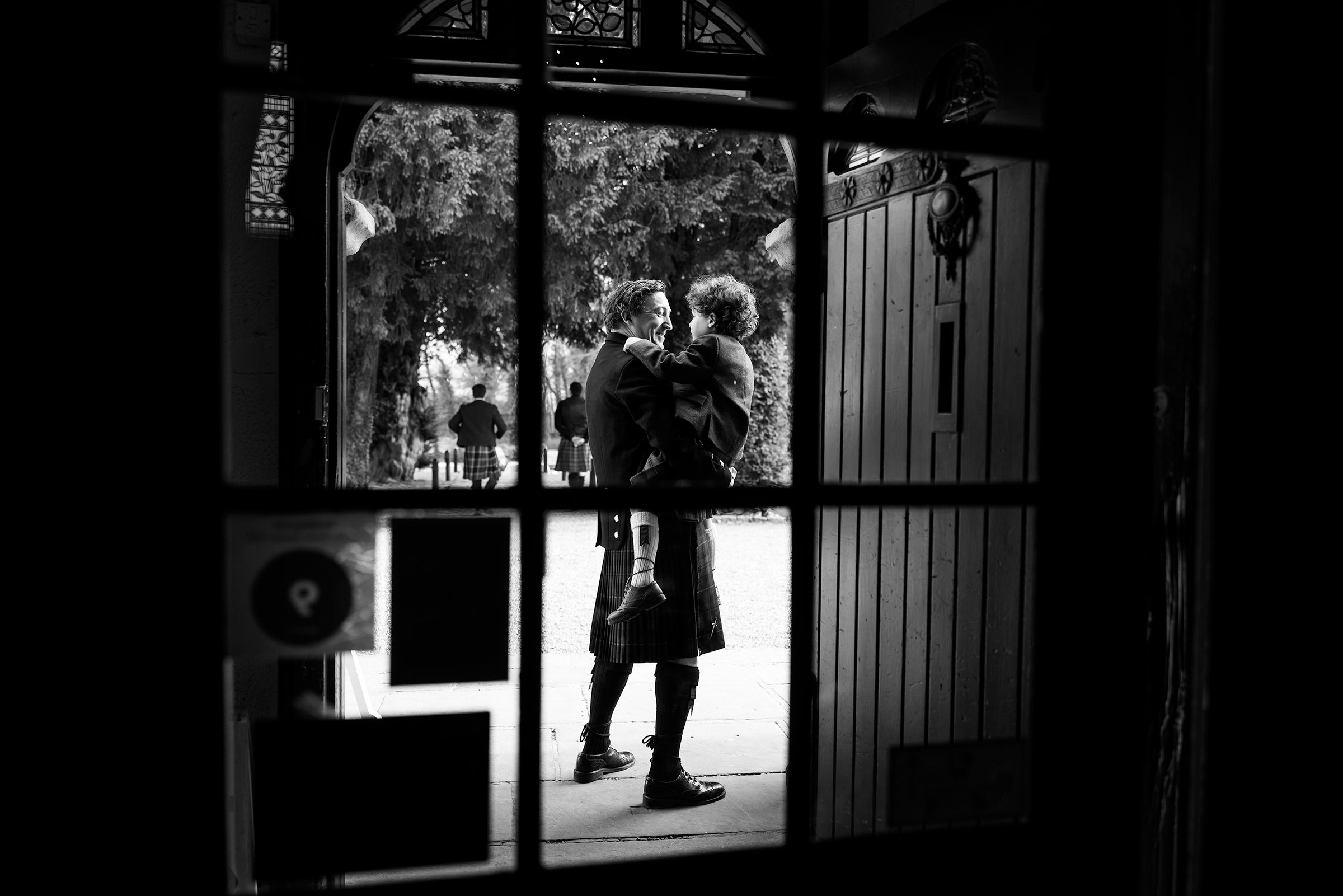 Black and white photo of two people embracing in a doorway, silhouetted against bright outdoor scenery.