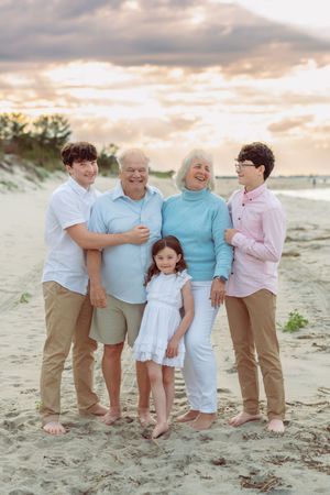 A family group poses together on a sandy beach at sunset wearing coordinated pastel blue and pink outfits.