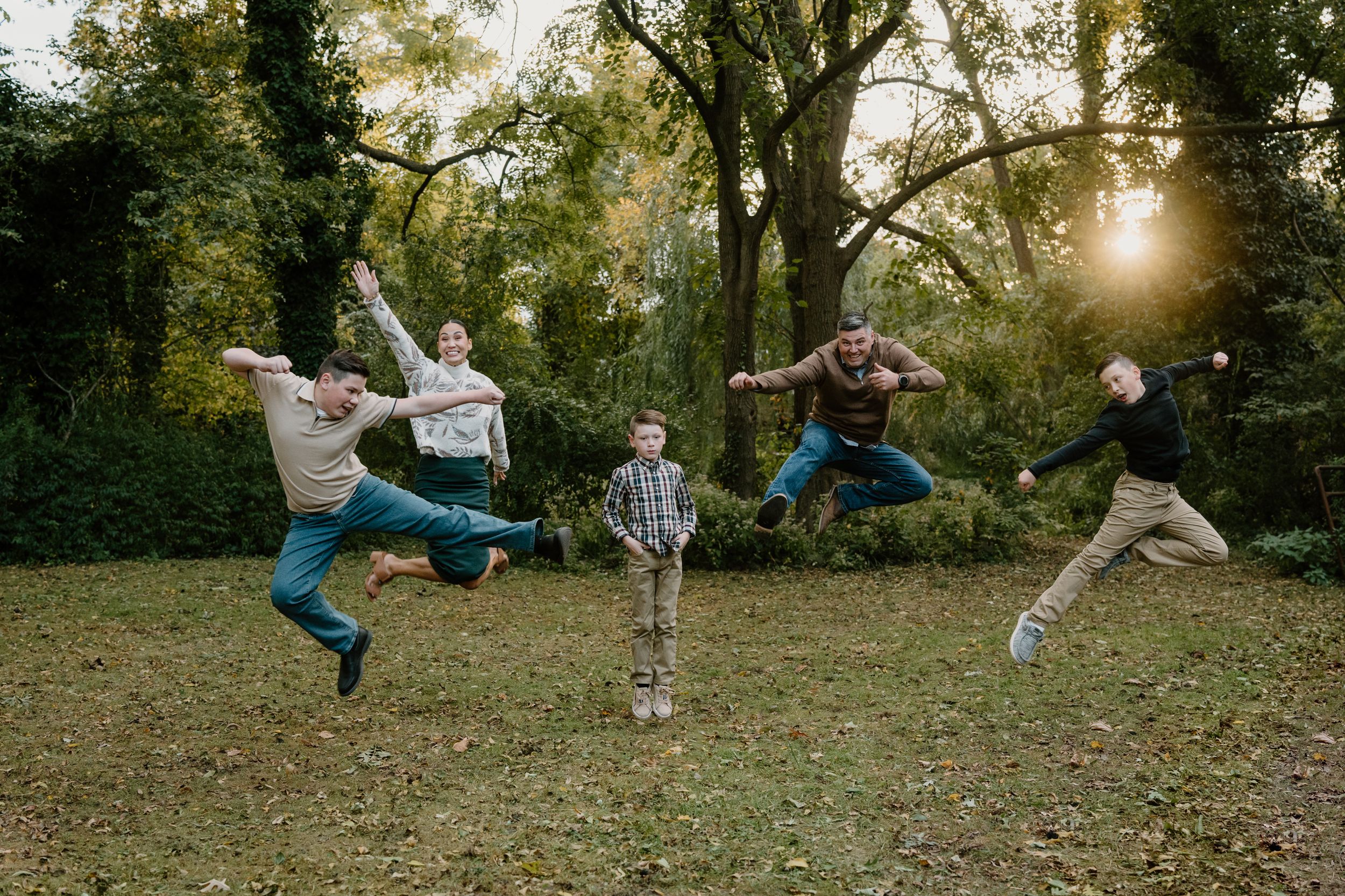 Five people leaping simultaneously in the air at a park during sunset.