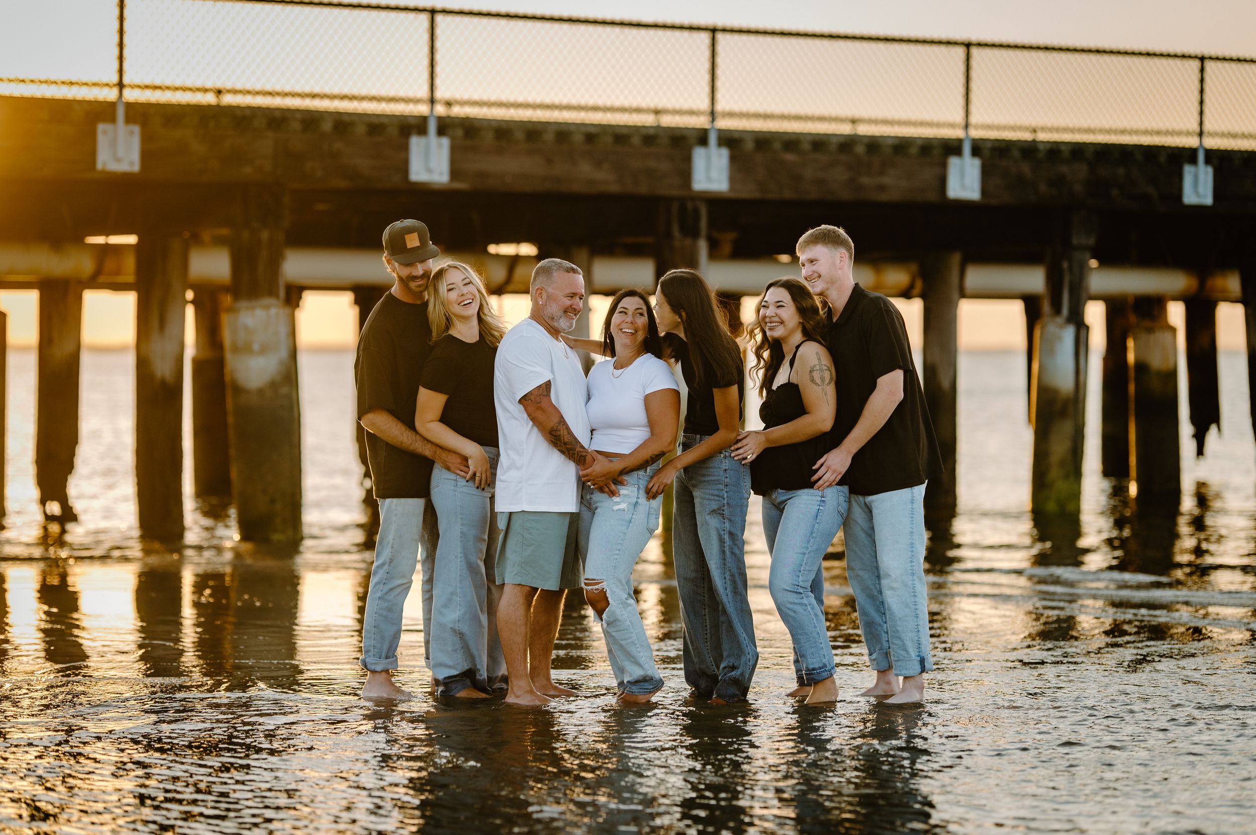 A group of people walking along a wooden boardwalk at sunset with reflections in the water below.