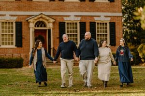 A group walks together on a lawn in front of a classic brick home with white trim during golden hour.