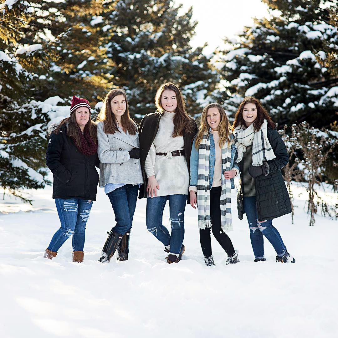 Five teenage girls posing together in winter coats in a snowy outdoor setting.
