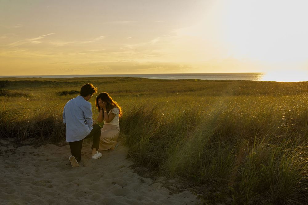 Couple walking hand in hand through golden sand dunes at sunset with ocean views.