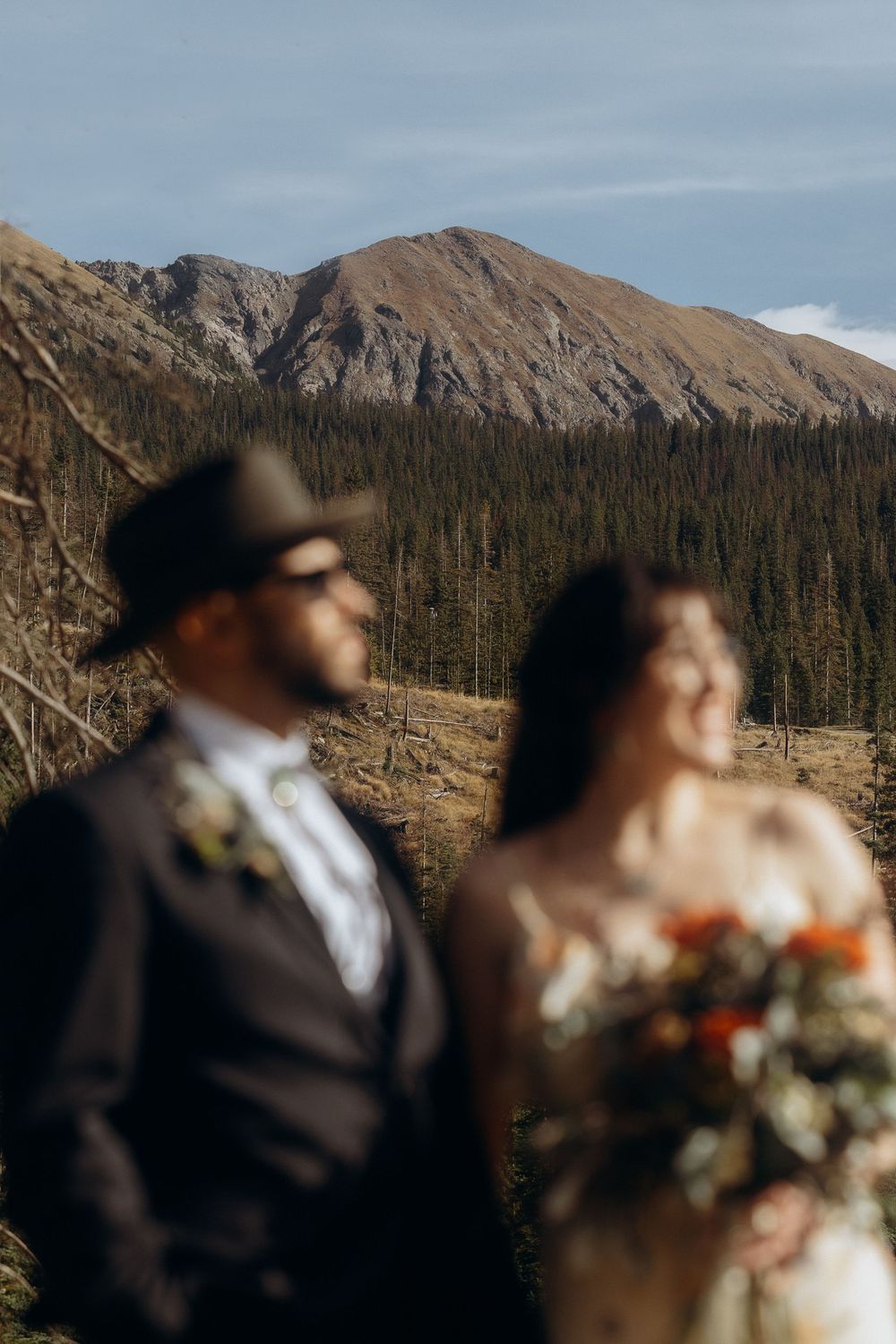 Blurred bride and groom pose before a stunning mountain landscape with pine forests during an outdoor wedding.