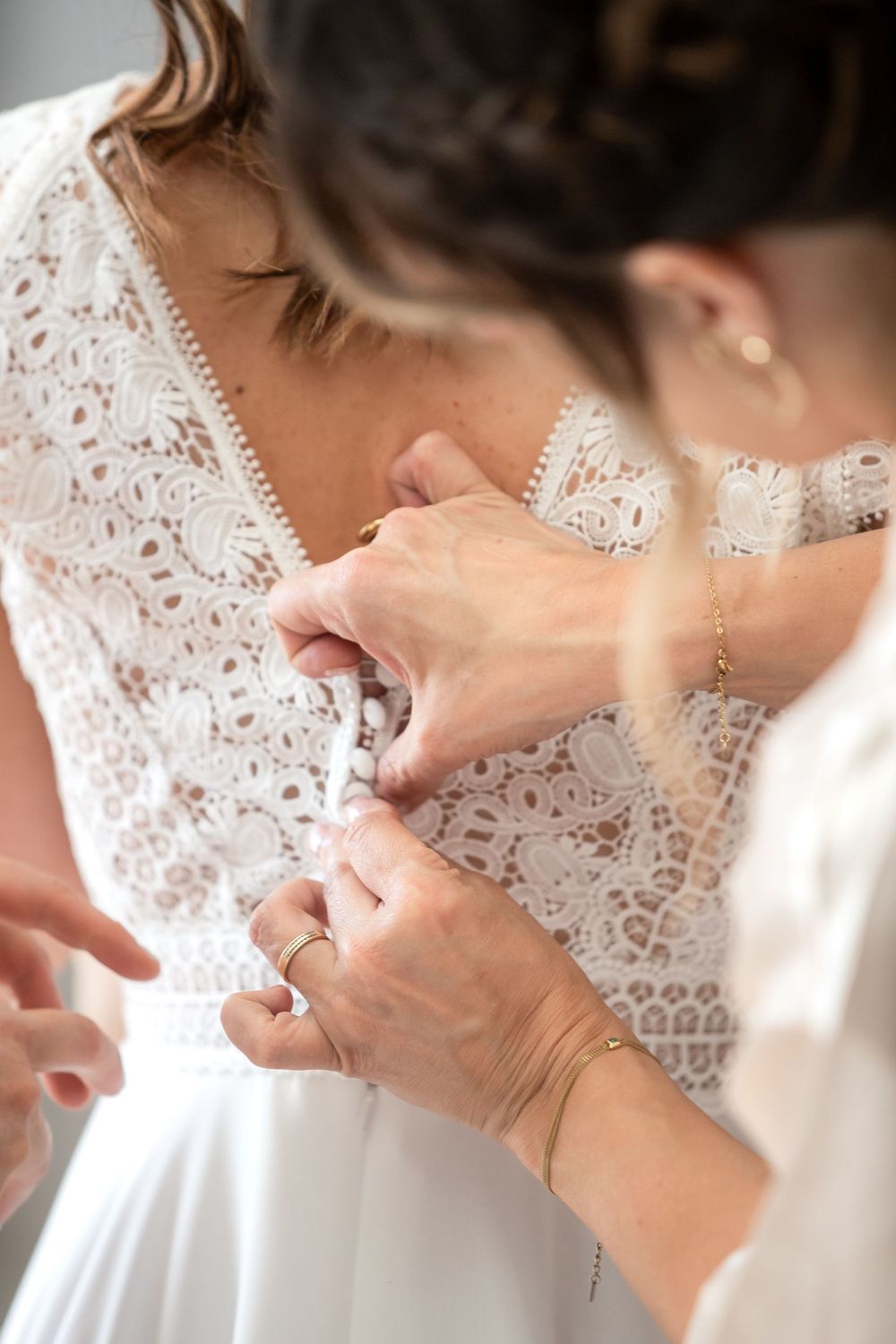 Bride getting her white lace wedding dress fastened by a helper during bridal preparations.