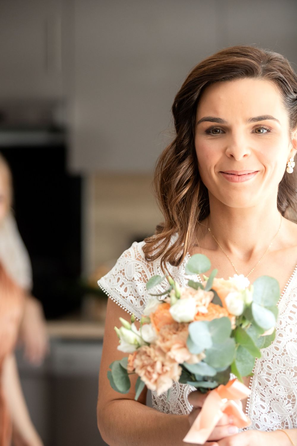 Smiling bride in white lace dress holding a bouquet of roses and eucalyptus on her wedding day.