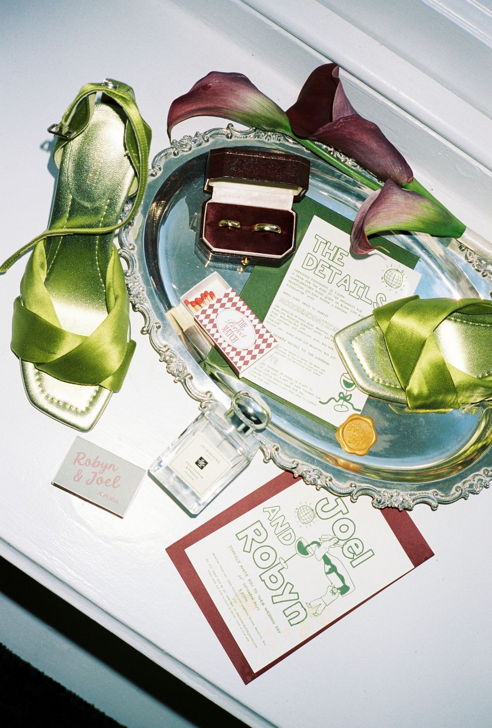Green satin heels, wedding rings in velvet box, calla lilies, and invitation suite for Robyn and Joel on silver tray.