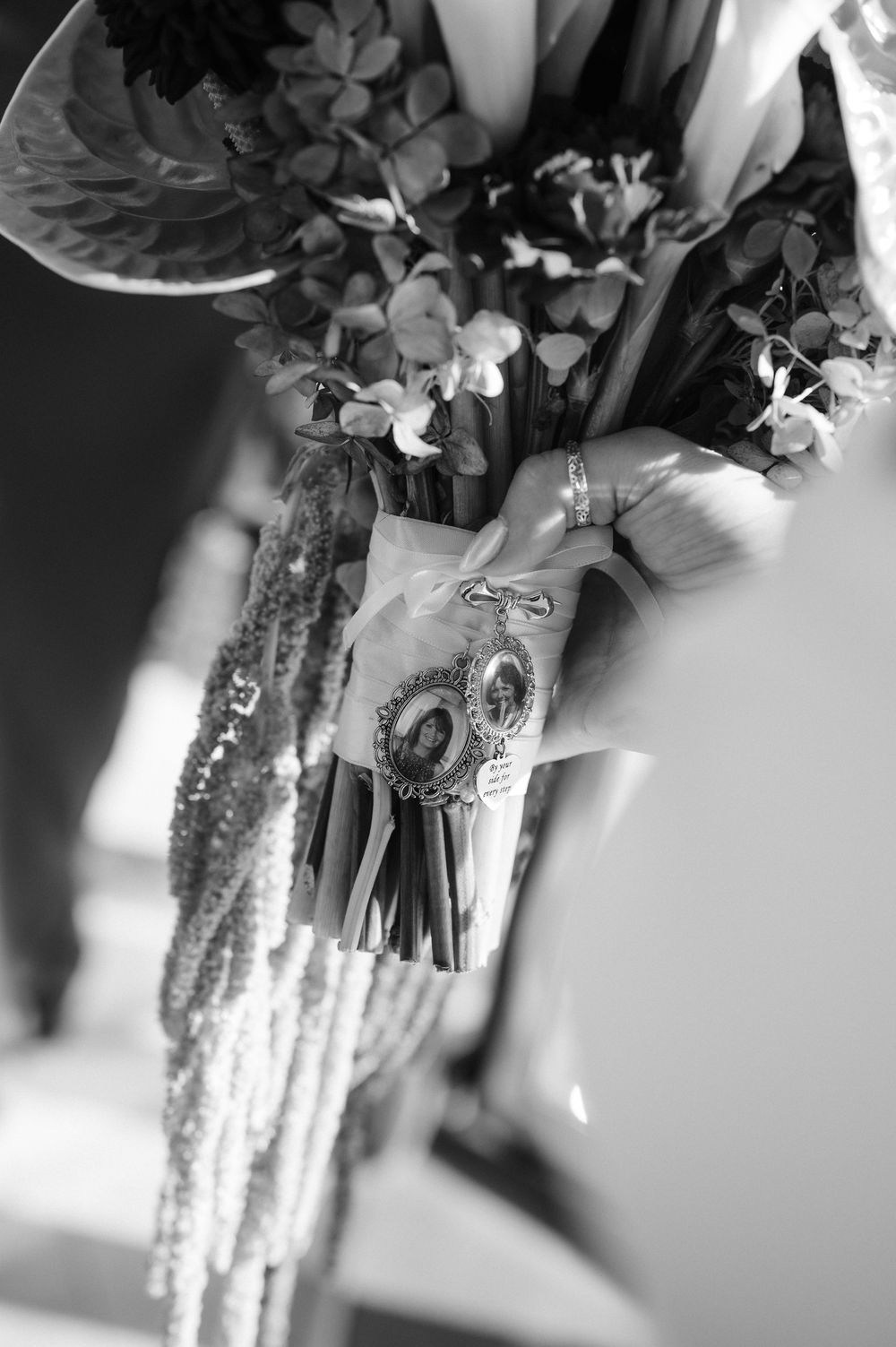 Black and white photo of a bridal bouquet with memorial photo charms and ribbon wrap detail.