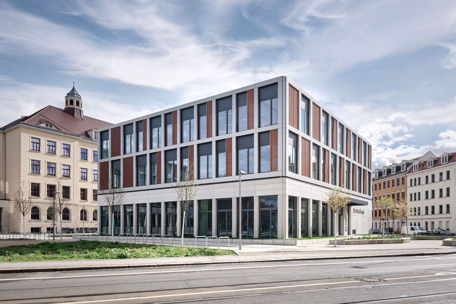 Modern multi-story office building with a brick and glass facade beside a historic clock tower building on a quiet city street.