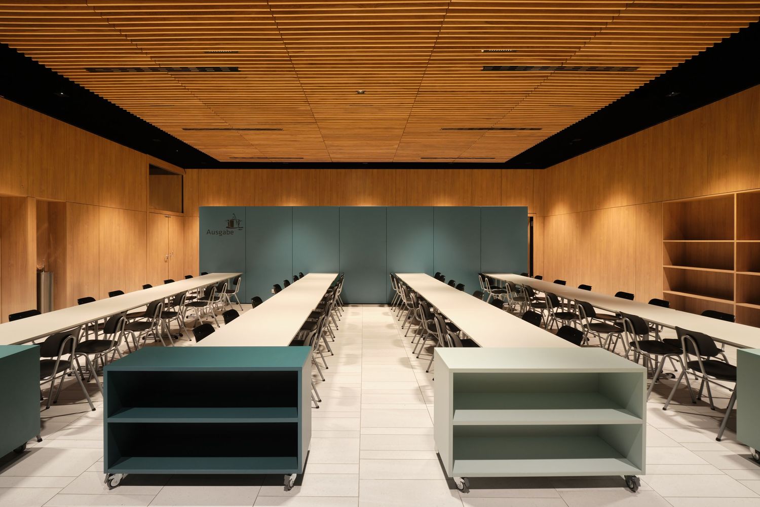 Modern meeting room with long white tables, black chairs, a wood slat ceiling, warm wood walls and teal rolling storage carts.