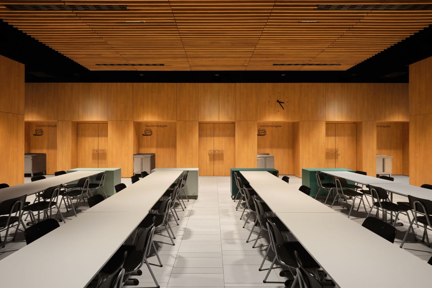 Modern conference hall with long white tables, black chairs, and warm wood-paneled walls and ceiling under soft recessed lighting.
