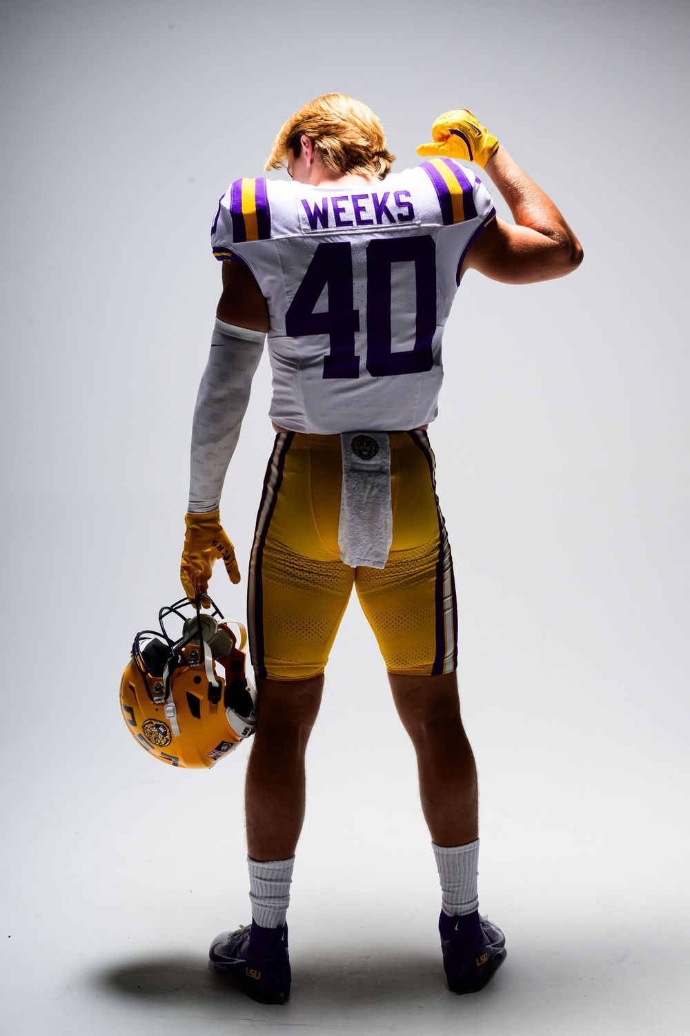 Football player seen from behind in a white number 40 Weeks jersey and gold pants, holding a gold helmet and adjusting his glove.