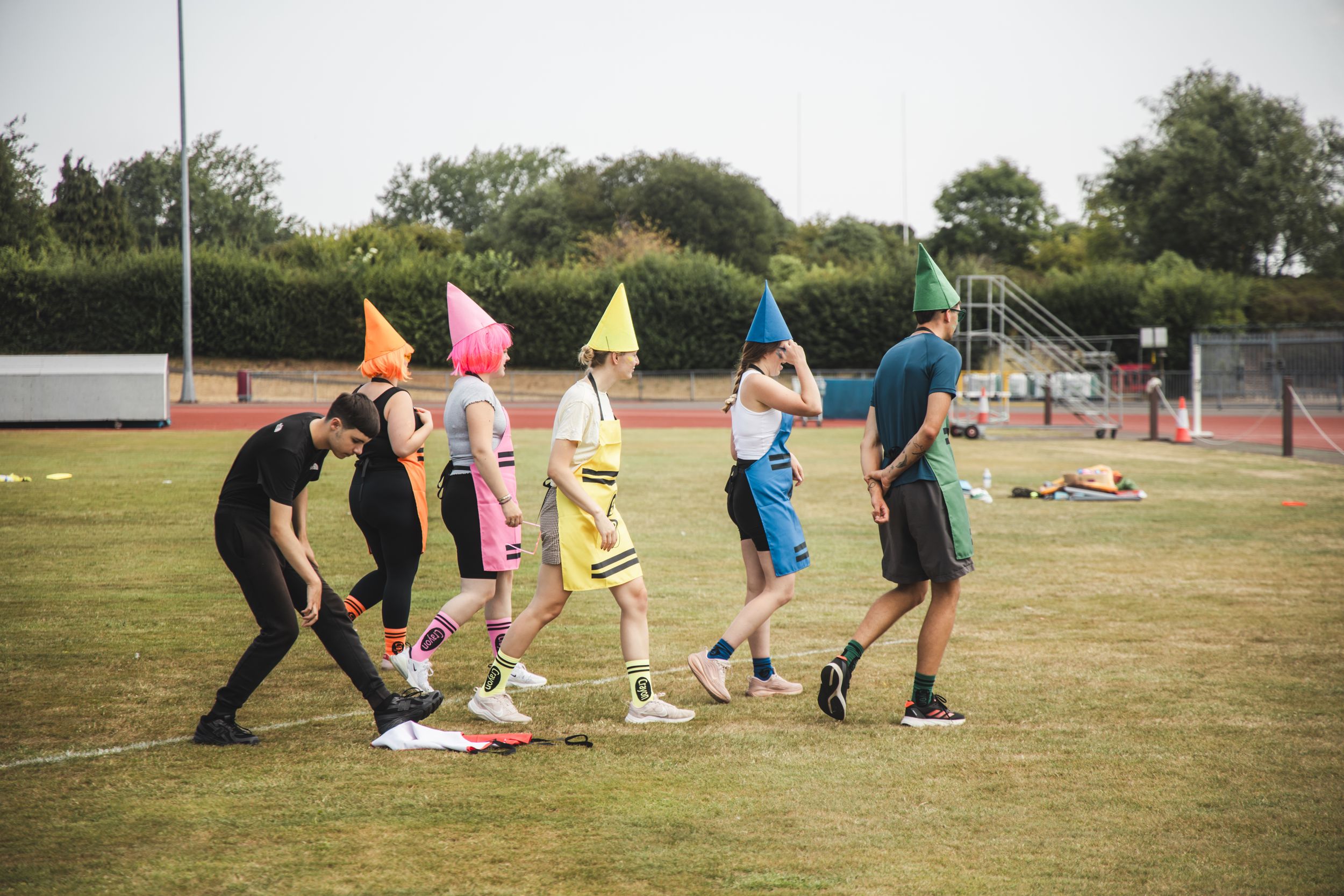 People wearing colorful cone hats play outdoor games on a sports field during a fun team activity event.