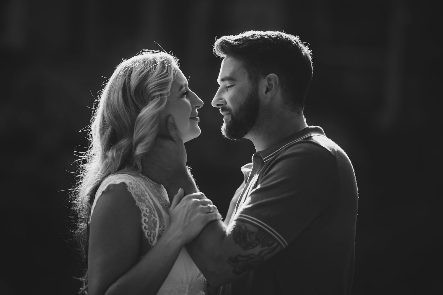 Black and white photo of a romantic couple gazing at each other, smiling and holding hands outdoors.