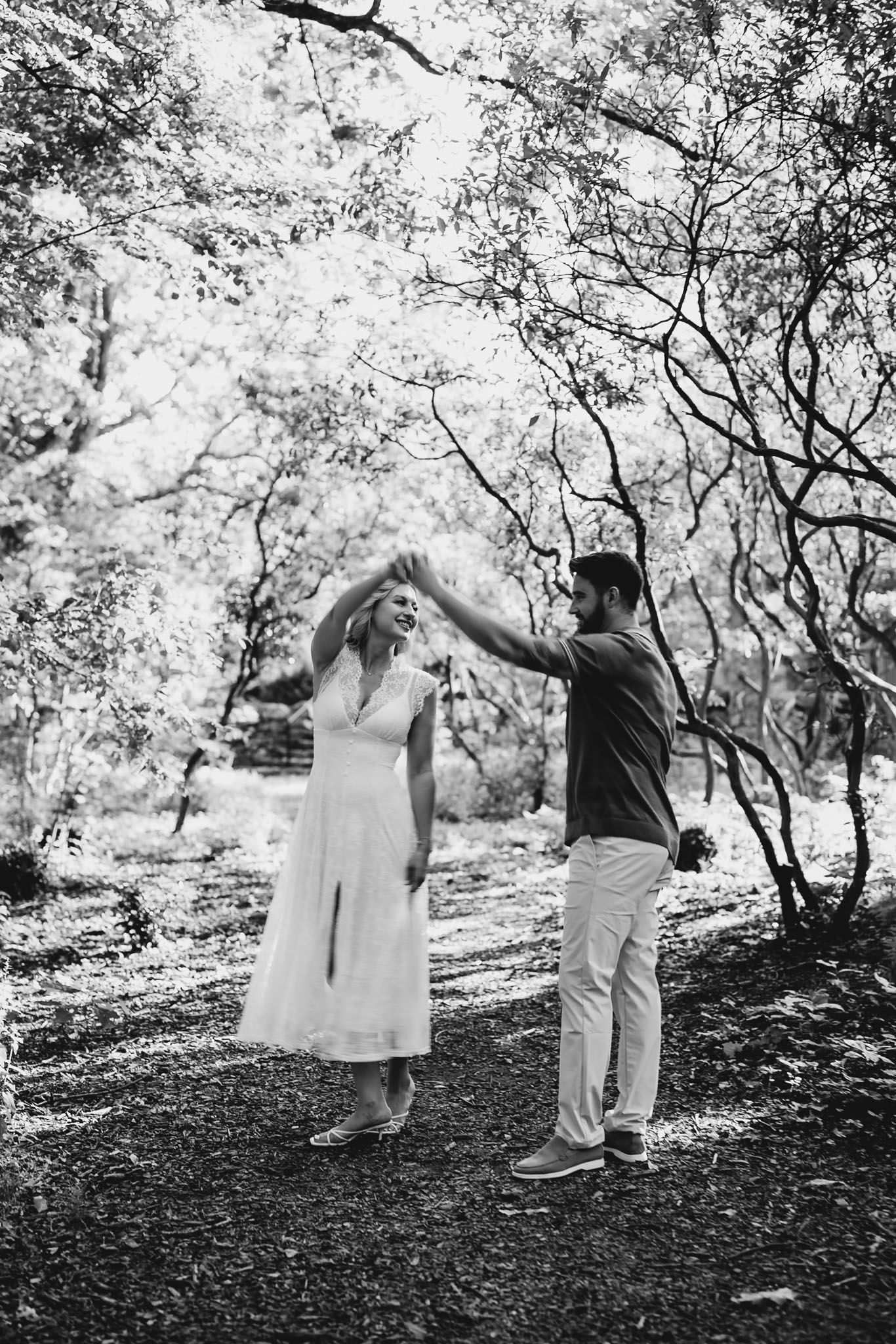 Couple dancing together in black and white photo among trees on a forest path.