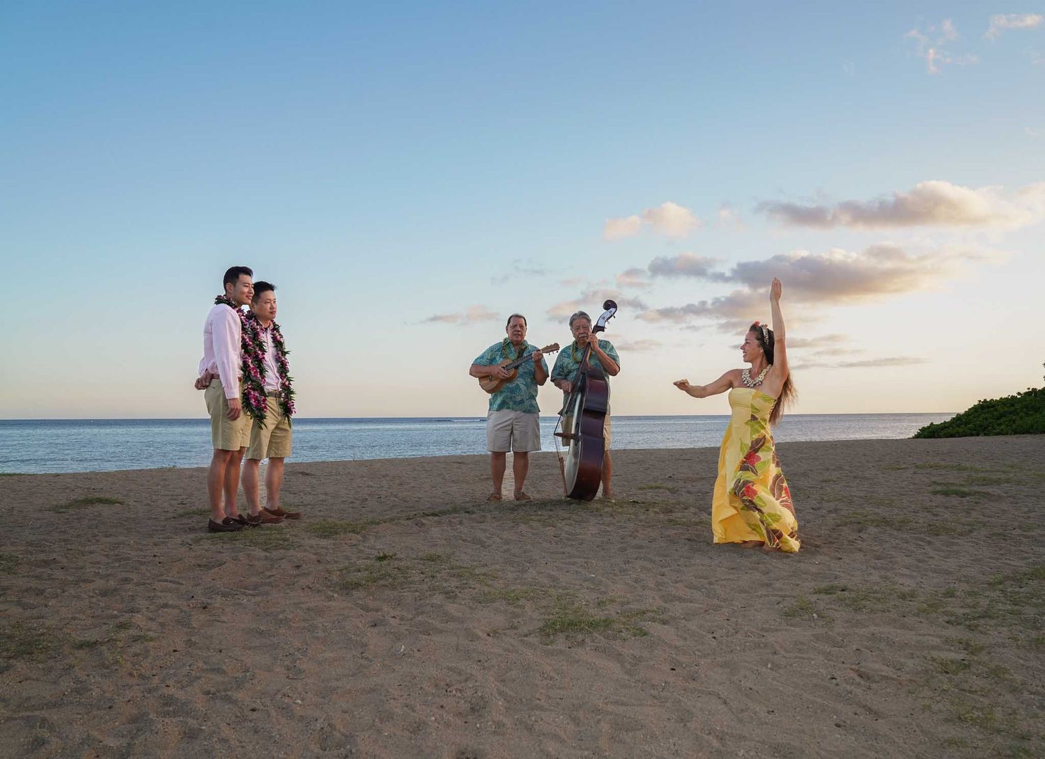 A woman in a floral dress dances on a beach at sunset while musicians play for a couple nearby.