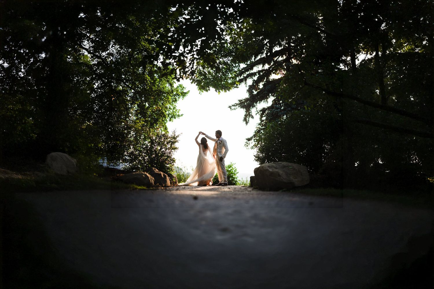 Groom twirling the bride at the bright end of a dark tree tunnel