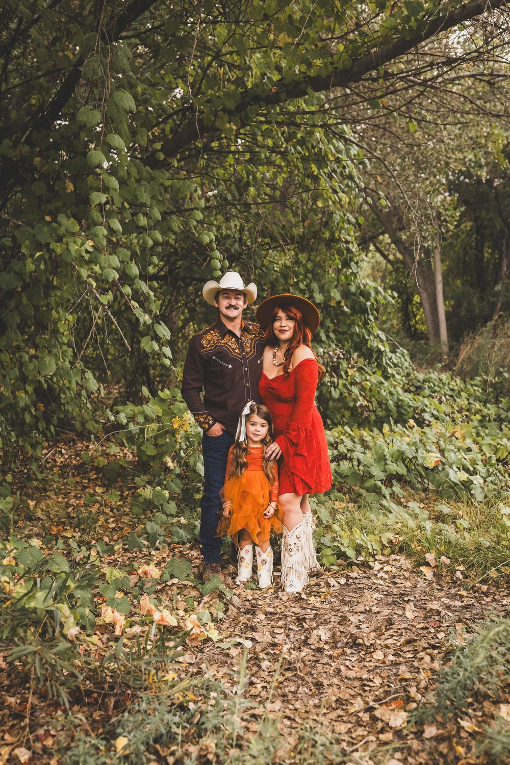 Family in western attire poses on a leaf-covered forest path in autumn.
