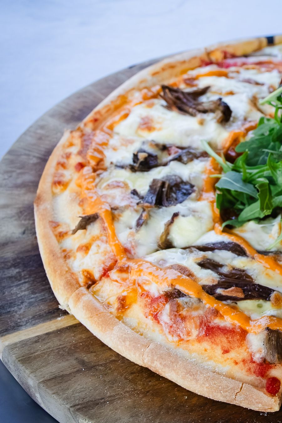 Freshly baked pizza with melted cheese, mushrooms, and arugula on a wooden serving board.