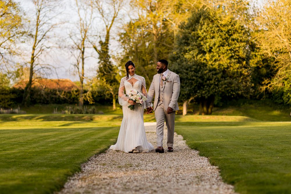 Bride and groom walking hand in hand along a gravel path surrounded by lush green gardens on their wedding day.