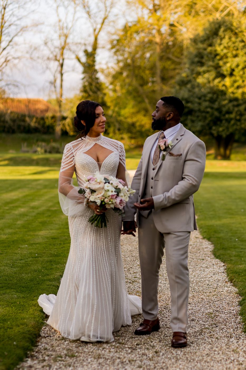 A bride and groom share a joyful moment on a gravel path surrounded by lush greenery on their wedding day.