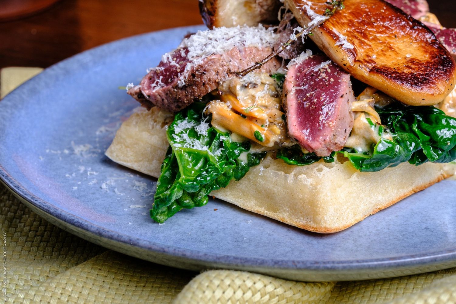 Gourmet seared duck breast sliced over creamy mushrooms and wilted spinach on flatbread, served on a rustic blue ceramic plate.
