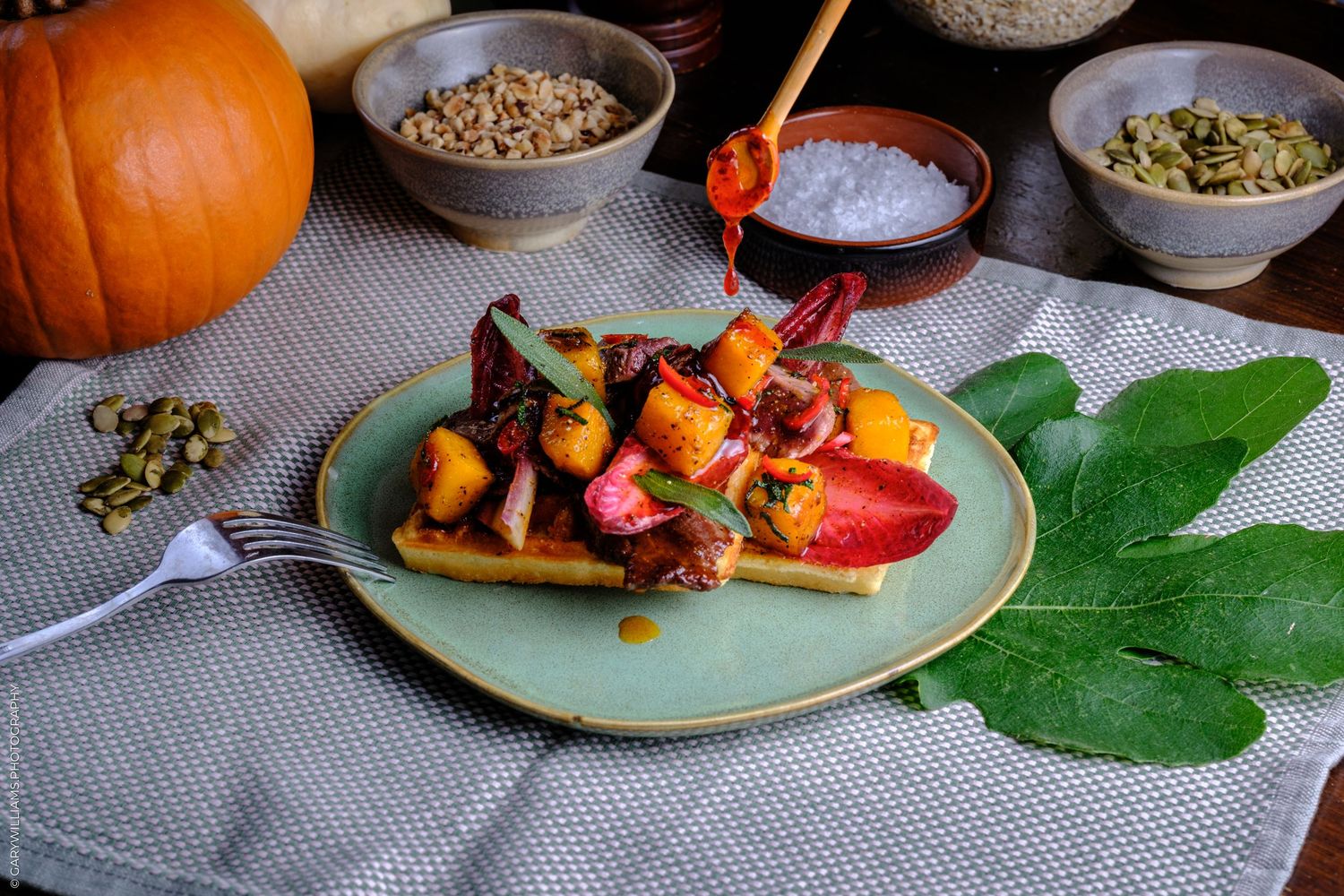 Autumn waffle topped with roasted pumpkin, beets, and fresh fruit on a green plate with pumpkin and seeds nearby.
