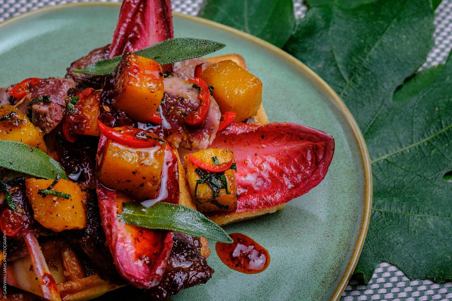 Colorful heirloom tomato salad with roasted butternut squash, fresh herbs, and balsamic glaze on a green ceramic plate.