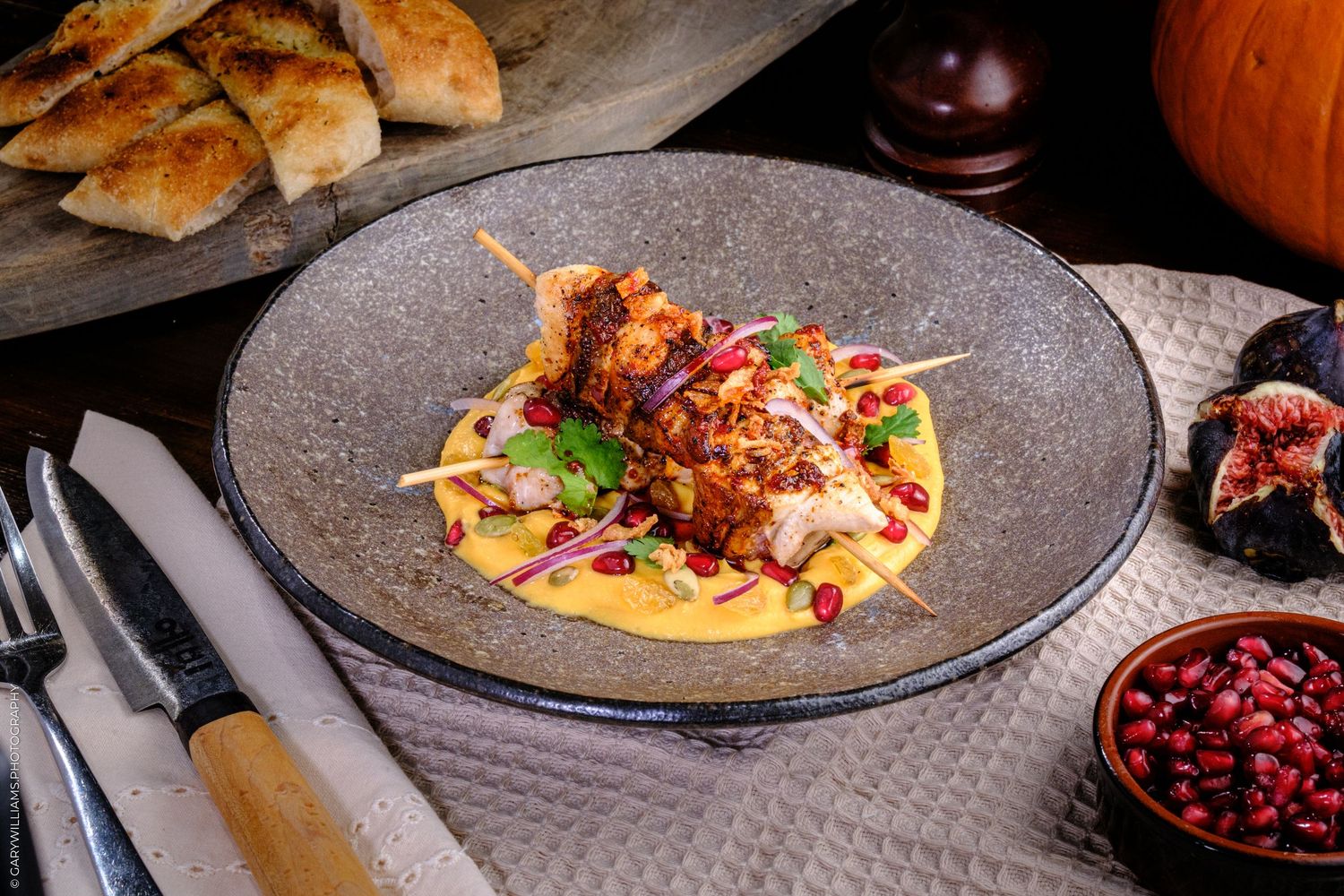 Grilled chicken skewer on saffron sauce with pomegranate seeds, served in a rustic gray ceramic plate.
