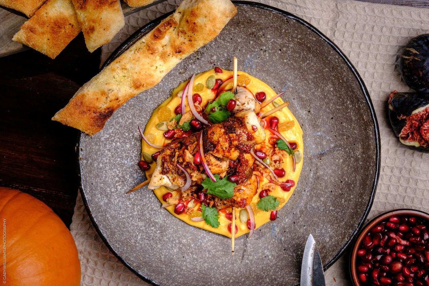 Elegant plate of spiced chicken over polenta with pomegranate, red onion, herbs, served with crispy flatbread on the side.