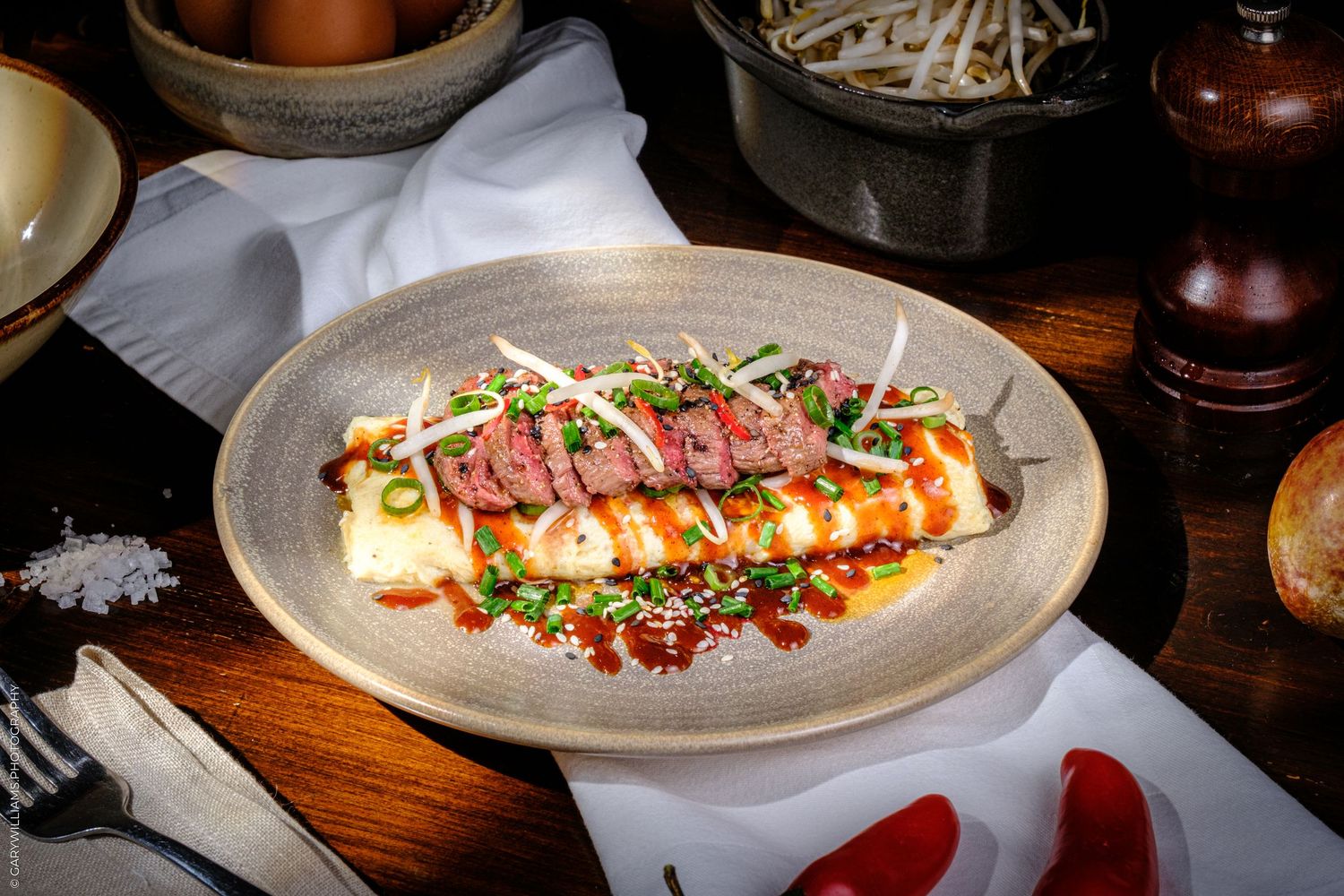Sliced beef steak served on creamy sauce with fresh herbs, microgreens, and drizzled sauce on an elegant ceramic plate.