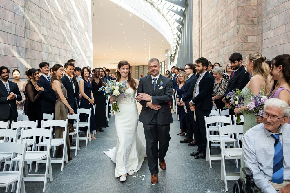 Bride walks down the aisle with her father at an elegant indoor wedding ceremony.