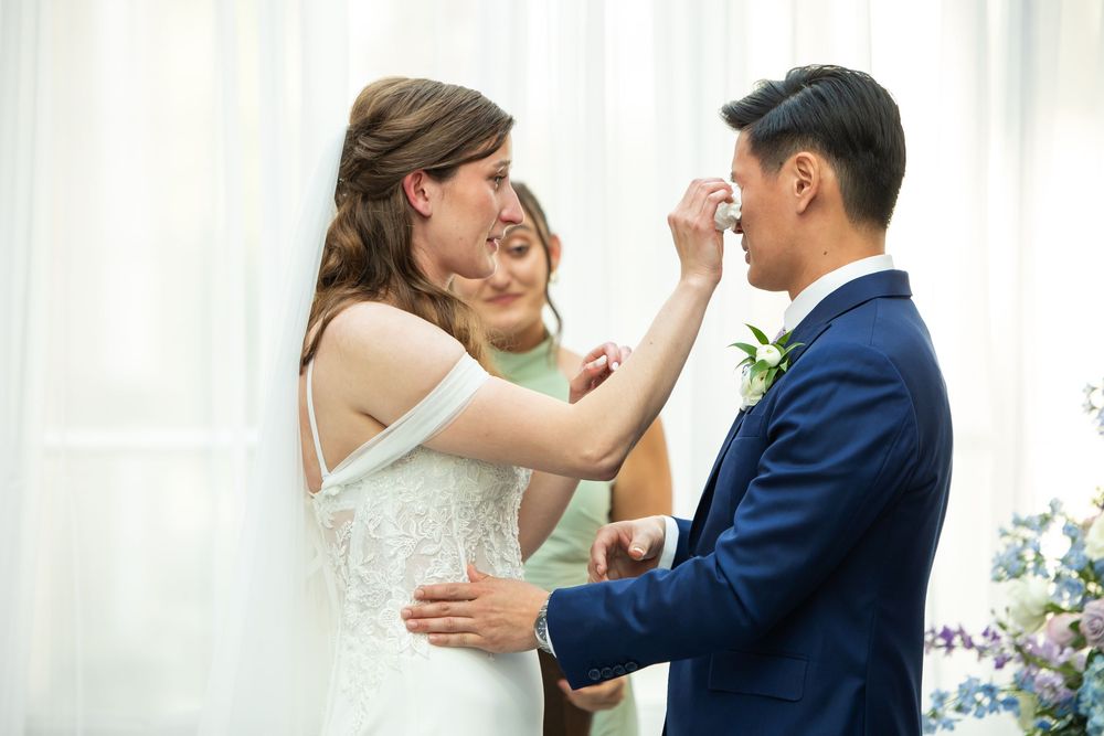 Bride tenderly touches grooms face during wedding ceremony with officiant in background.