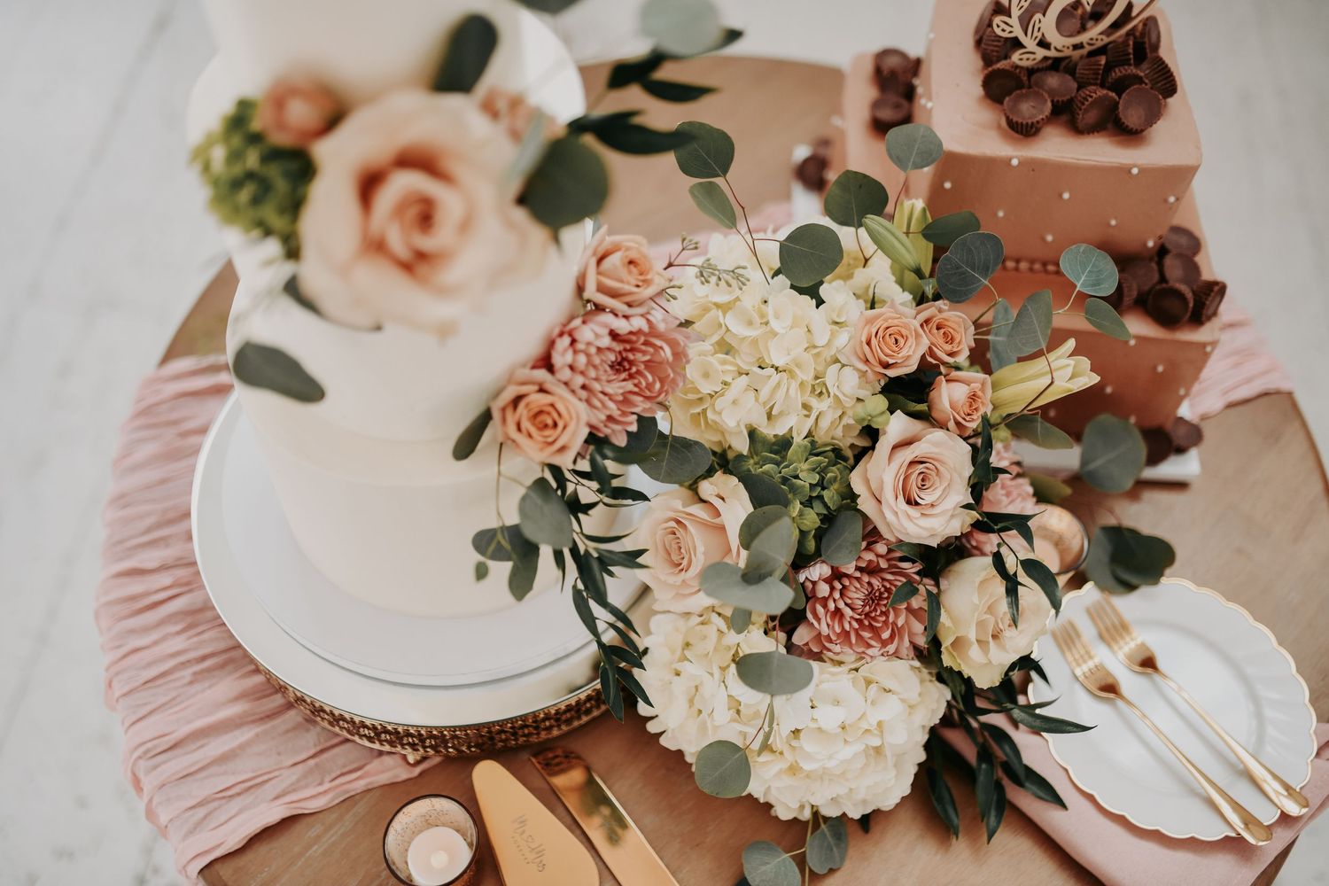 Three-tier wedding cake surrounded by blush roses, hydrangeas and greenery