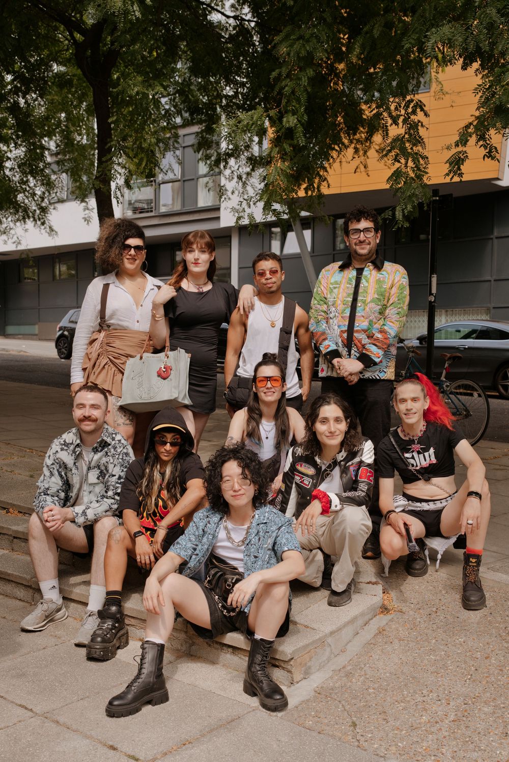 A diverse group of ten stylishly dressed young people posing together on outdoor steps near a tree.