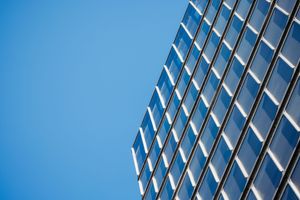 Modern glass office building facade reflecting blue sky, showcasing sleek architectural design and urban corporate aesthetic.