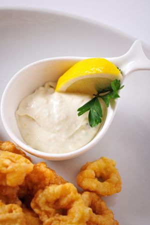 Crispy fried calamari rings served with creamy tartar sauce, fresh parsley, and a lemon wedge on a white plate.