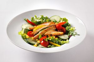Fresh grilled chicken salad with cherry tomatoes, cucumber, mixed greens, and colorful vegetables served on a white plate.