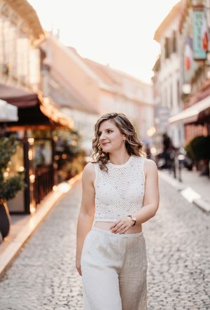 Young woman in white knit crop top and linen pants walking on cobblestone street at golden hour.
