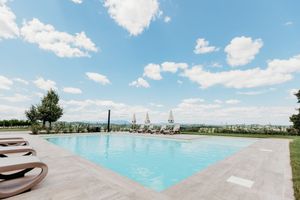 Luxury outdoor swimming pool with lounge chairs and umbrellas overlooking a scenic countryside landscape under blue sky.