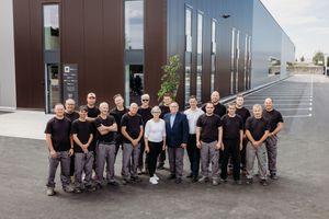 Group of employees in black uniforms posing outside a modern industrial building for a team photo.