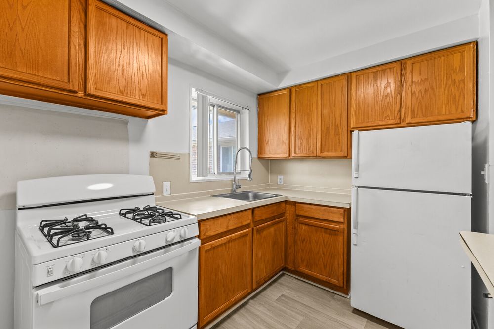 Compact kitchen featuring honey oak cabinetry, white gas stove, refrigerator, and sink with natural window light.