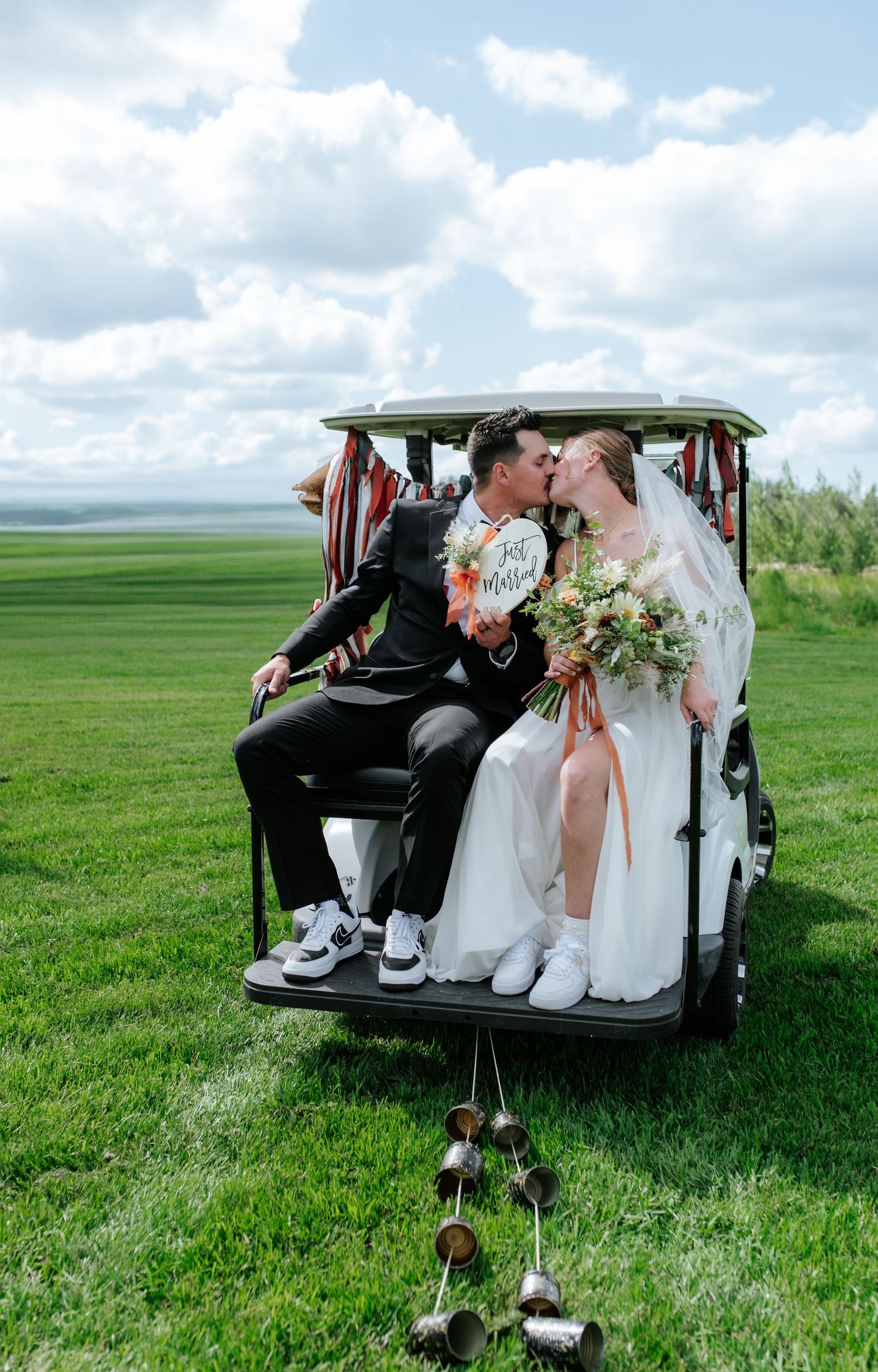 Black and white photo of a bride and groom kissing under a wedding veil outdoors.