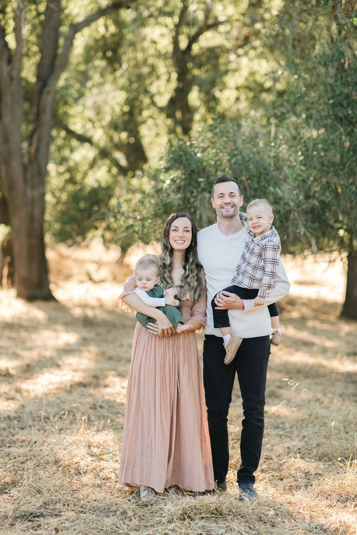A couple embraces while sitting in the branches of a large oak tree surrounded by golden grass.