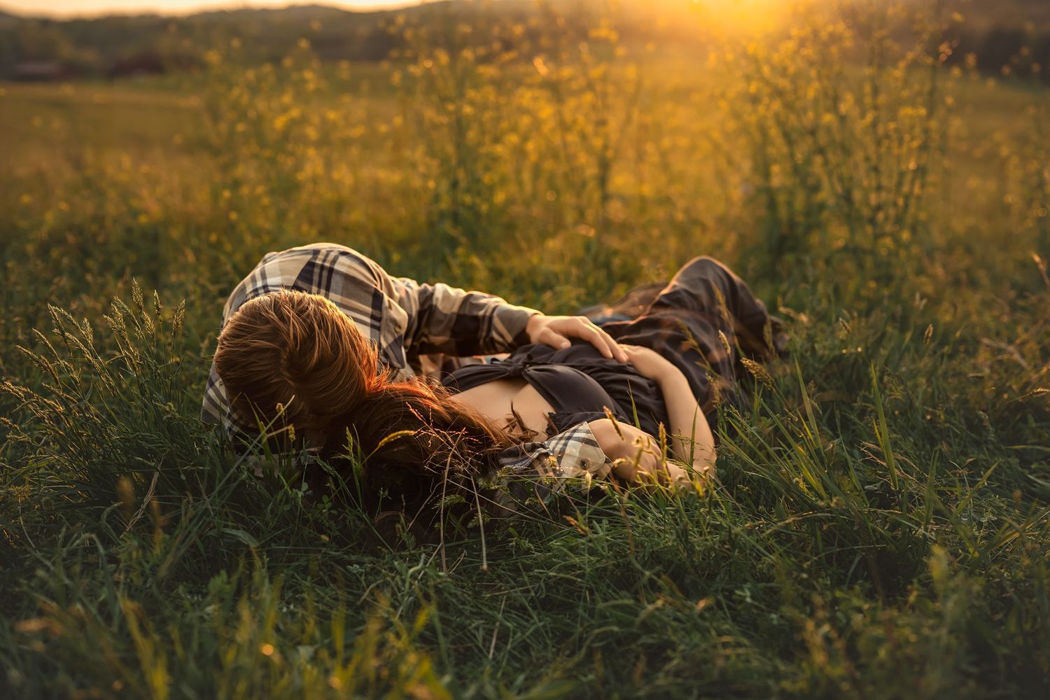 Pregnant couple cuddles together lying in golden wildflower meadow grass during warm sunset light for maternity photos in atlanta